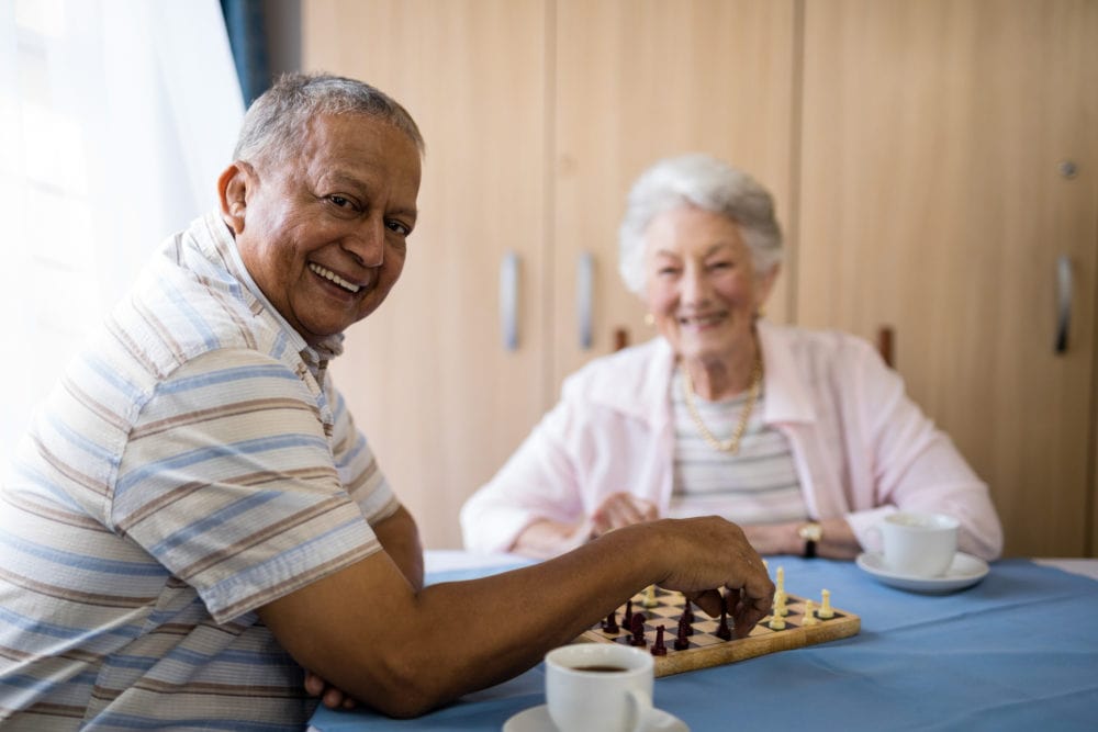 Smiling senior man playing chess with friend while sitting at table in nursing home