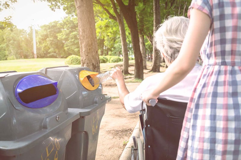 A photo of a senior woman in a wheelchair, recycling a water bottle.