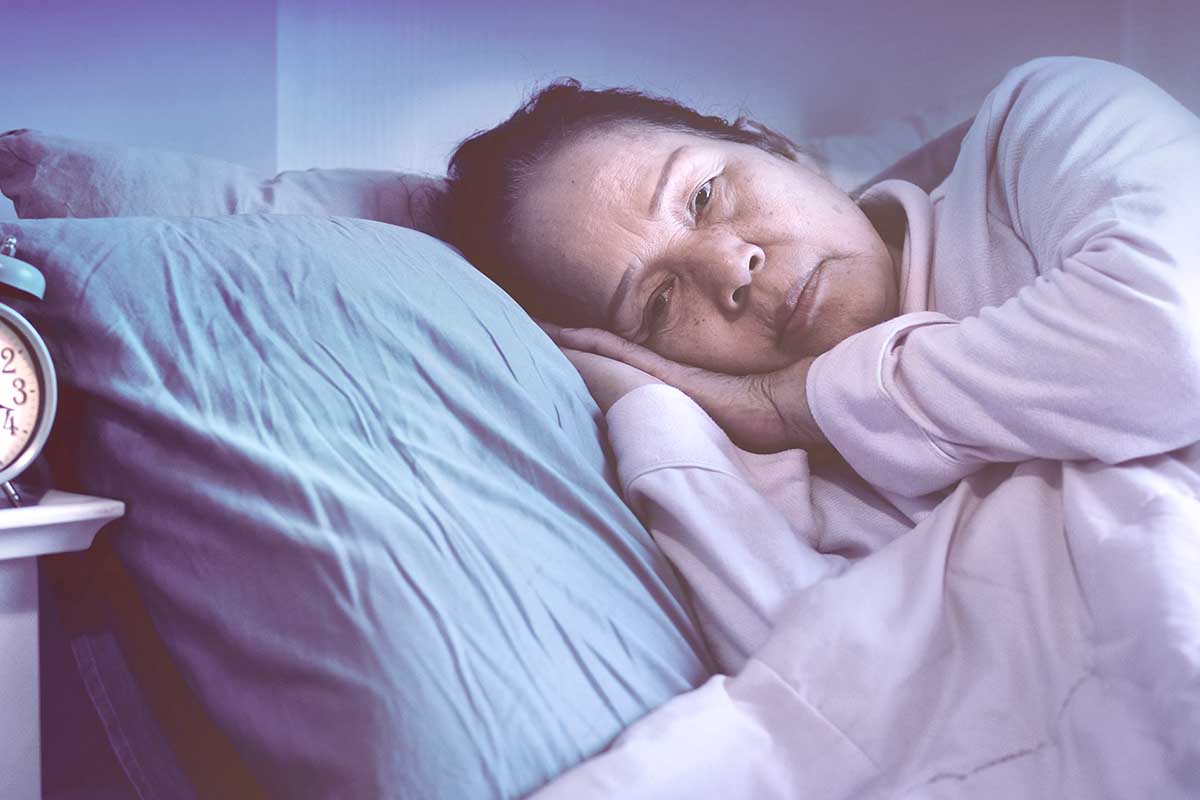 A photo of a senior woman lying awake in bed at night.
