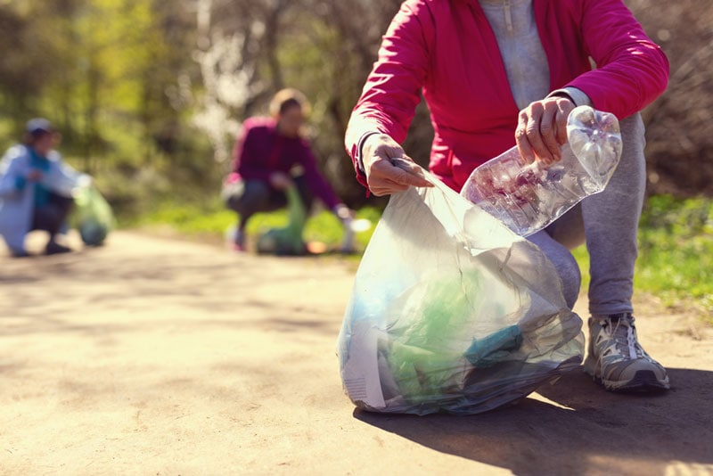 Kind eco-friendly volunteers holding packets and gathering garbage