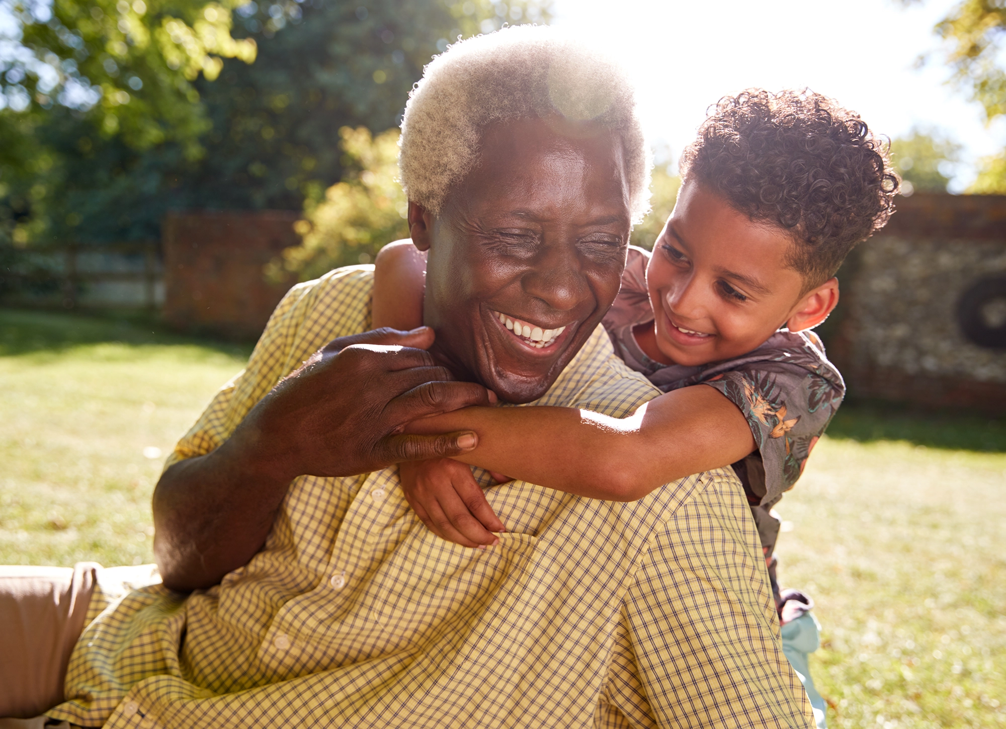 Senior man and his grandson hugging each other while smiling and playing in the grass