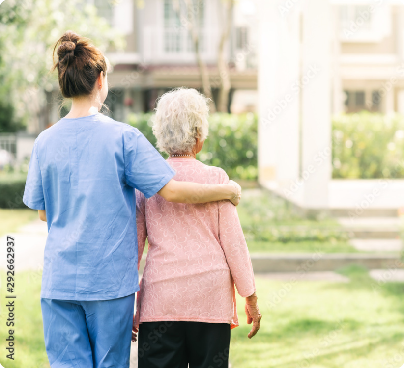 A nurse in scrubs helping a tapestry memory care resident at SALMON Health and Retirement walk outside