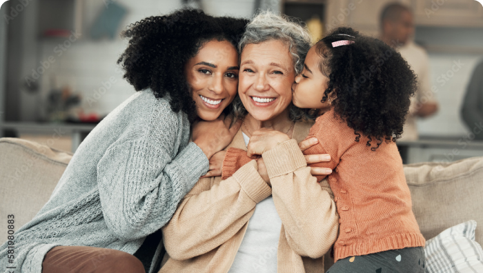 Elder daughter, granddaughter and grandmother hugging each other on a couch