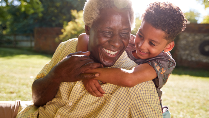 Senior man and his grandson hugging each other while smiling and playing in the grass