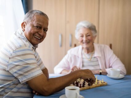 Smiling senior man playing chess with friend while sitting at table in nursing home