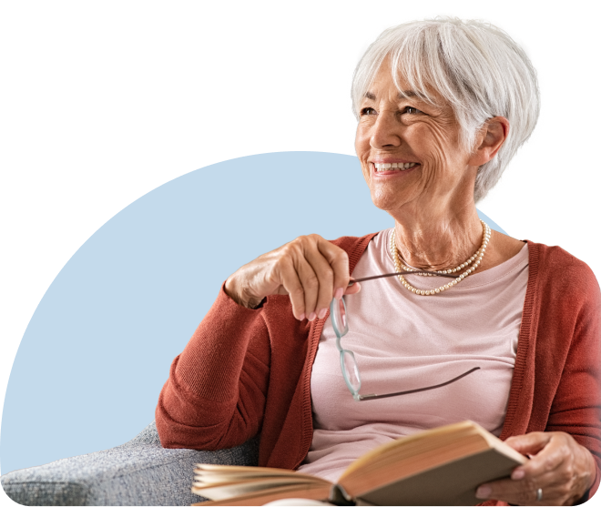 Senior woman smiling while reading a book at home, holding reading glasses – elderly lifestyle, relaxation, and wellness concept.