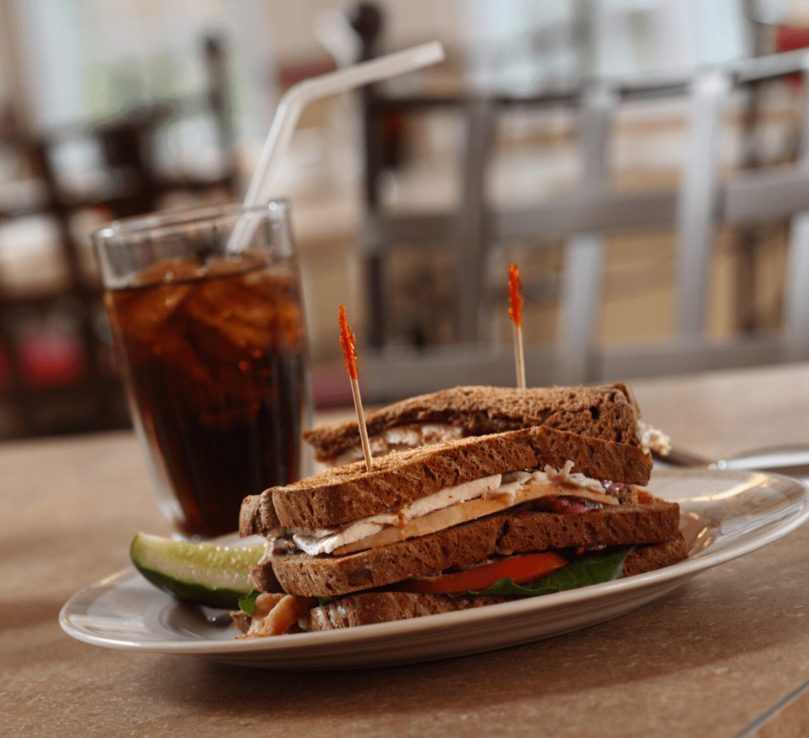 Turkey on wheat bread sandwich with a pickle and cola