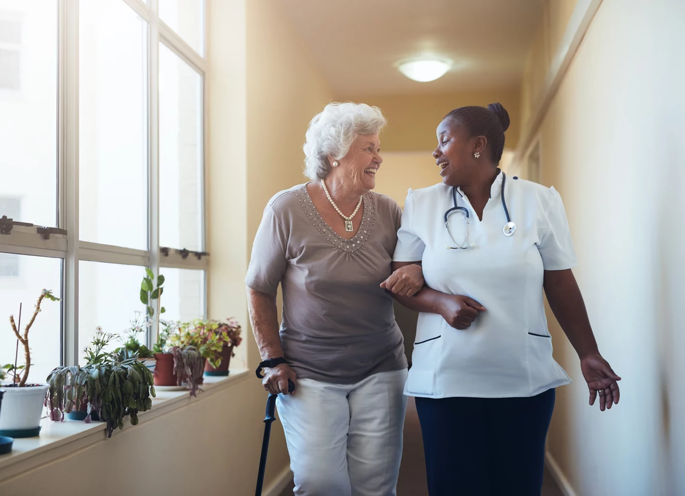 A nurse helping a senior women walking down the hall of SALMON's Beaumont Assisted Living and Rehabilitation community
