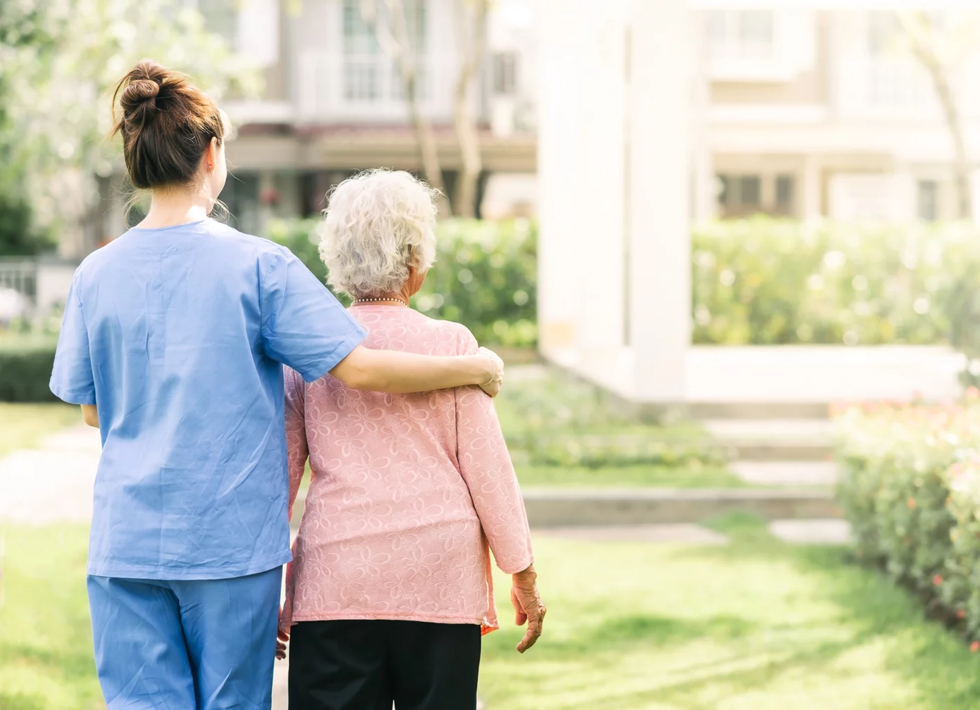 A nurse in scrubs helping a tapestry memory care resident at SALMON Health and Retirement walk outside