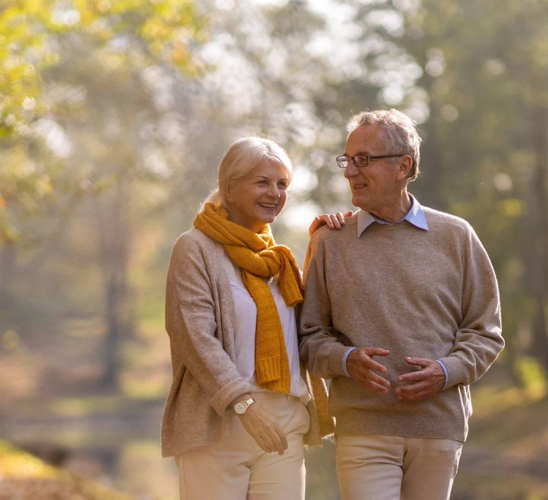 Senior couple walking outside in the sunshine near trees